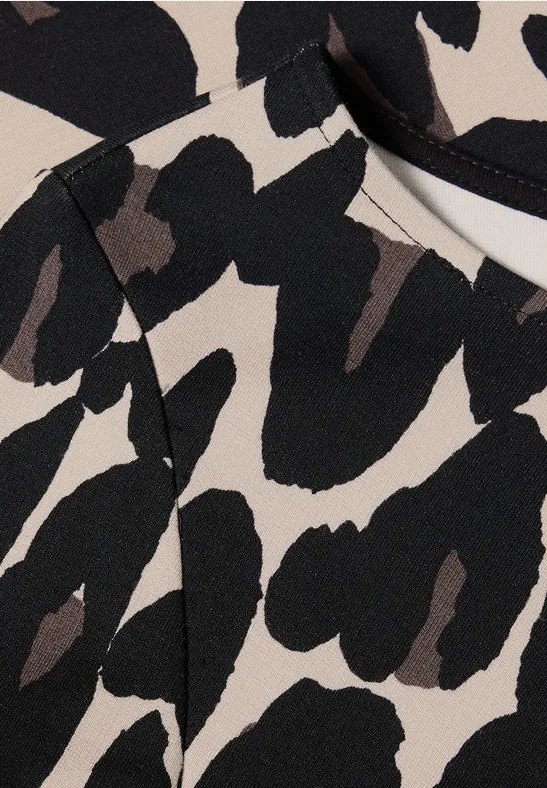 Abstraktes Stoffmuster in Beige mit großen, unregelmäßigen schwarzen Flecken, erinnert an Leopardenprint.
