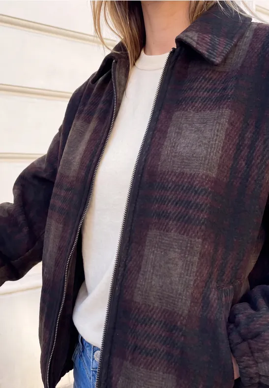 Person trägt dunkle karierte Jacke über weißem Shirt und Jeans