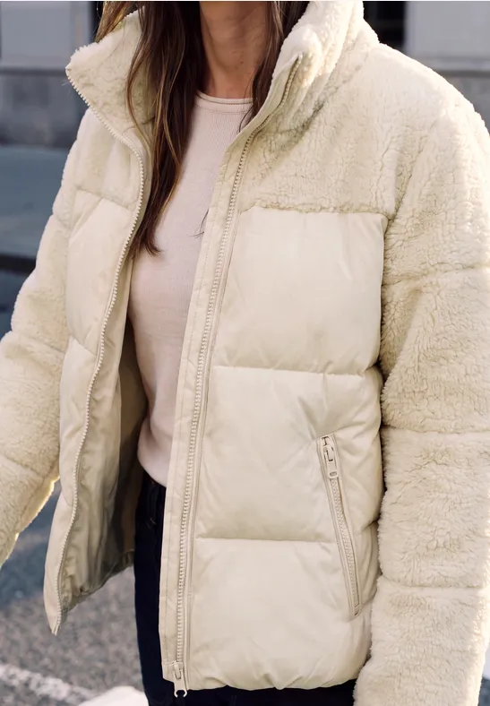 Nahaufnahme einer Person im cremefarbenen Steppjacke mit Teddyfleece-Details.