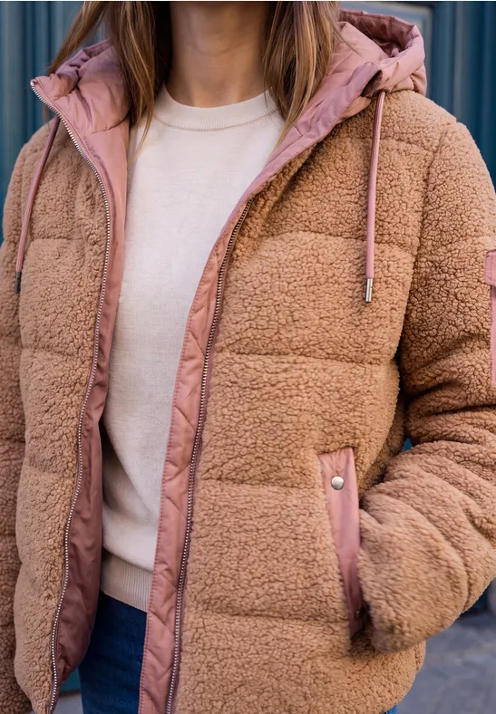 Nahaufnahme: Person trägt beigen Teddy-Puffer mit rosa Futter, Kapuze, weißes T-Shirt und Jeans.
