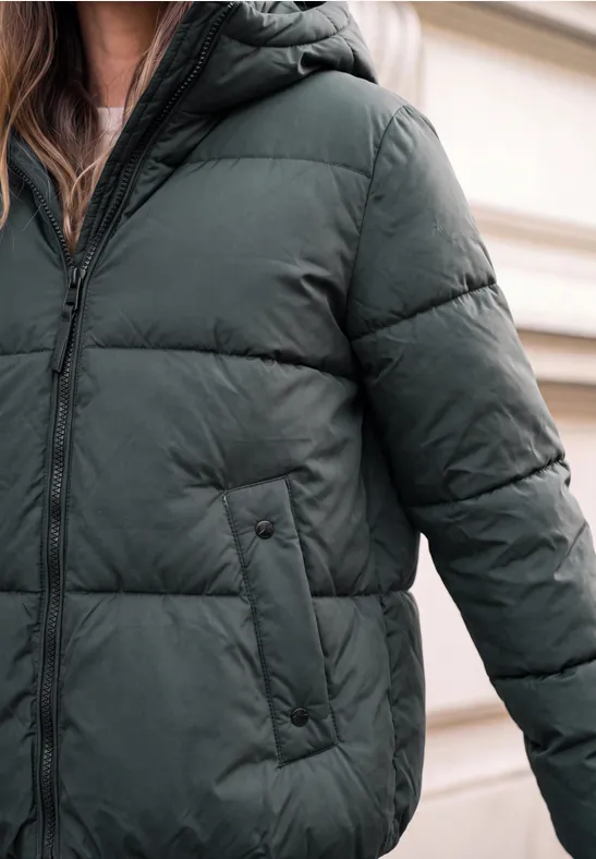 Person trägt eine dunkelgrüne Daunenjacke mit Reißverschluss und seitlichen Taschen im Nahaufnahme.