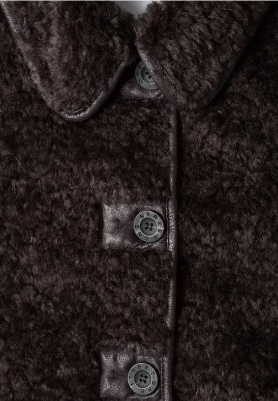 Zbliżenie brązowego płaszcza teddy z puchatą fakturą i widocznymi guzikami.