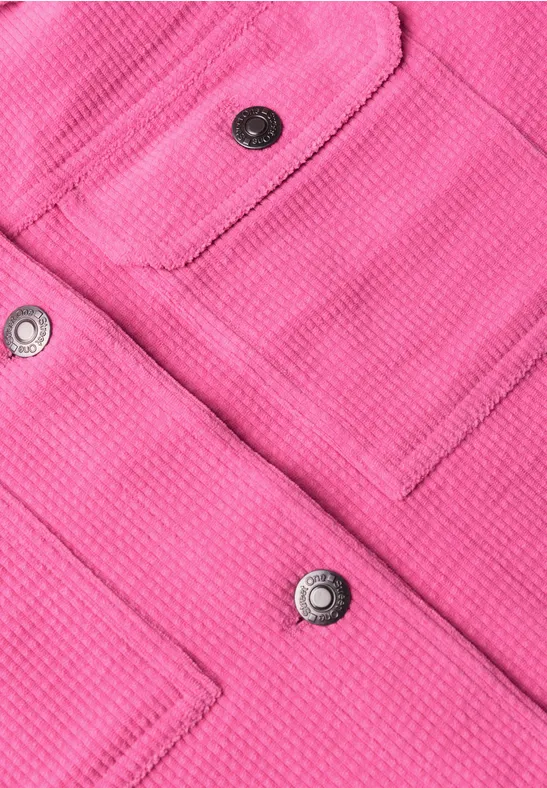 Nahaufnahme eines pinken Stoffes mit aufgesetzten Taschen und silbernen Druckknöpfen.