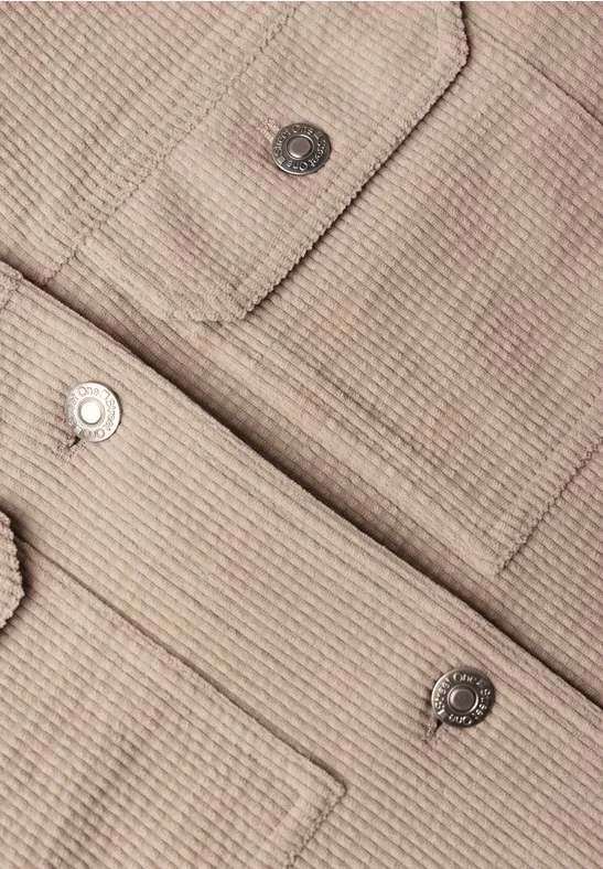 Nahaufnahme einer beige strukturierten Jacke mit aufgesetzten Taschen und silbernen Druckknöpfen.