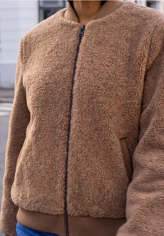 Person trägt eine braune Teddy-Fleecejacke mit Reißverschluss und seitlichen Taschen.