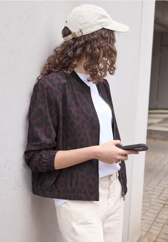 Een persoon met witte pet, een patroonjas en een smartphone leunt ontspannen tegen een muur.