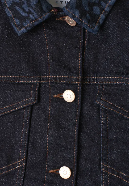 Nahaufnahme einer blauen Jeansjacke mit kontrastierenden orangefarbenen Nähten und hellen Knöpfen.