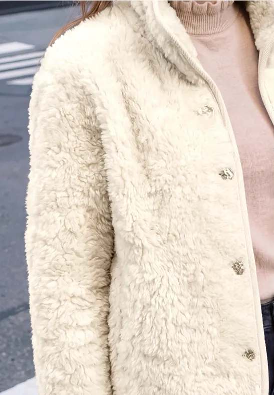 Person trägt eine cremefarbene Teddyjacke mit Druckknöpfen und einen rosafarbenen Rollkragenpullover.
