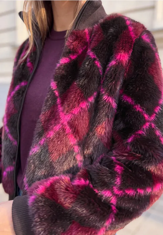 Person trägt rosa-braune Karojacke aus Kunstfell über violettem Pullover.