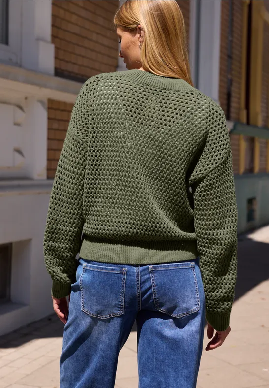 Frau von hinten in grünem Strickpullover und Jeans, spazierend auf sonnigem Bürgersteig.