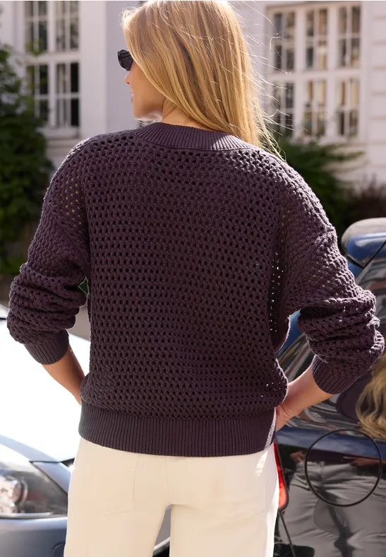 Blonde Frau von hinten in dunkelviolettem Strickpullover und weißen Hosen neben Autos.