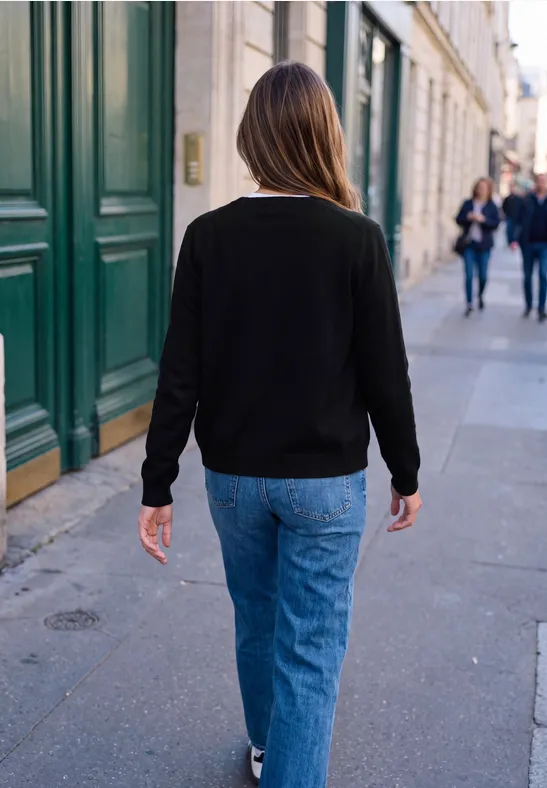 Eine Person in schwarzem Pullover und Jeans geht auf dem Bürgersteig an Häusern vorbei.
