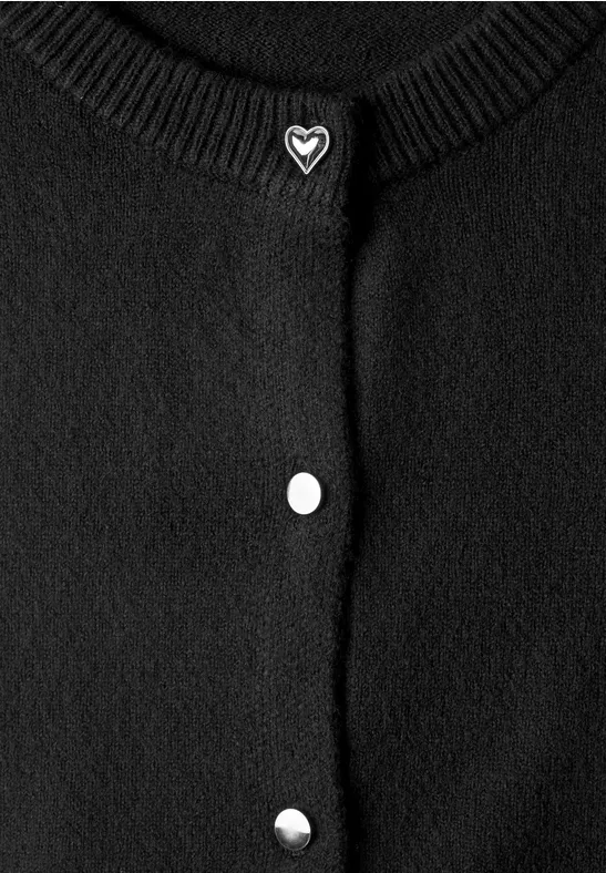 Schwarze Strickjacke mit Rundhalsausschnitt, drei silberne Druckknöpfe und herzförmiger Brosche am Kragen.