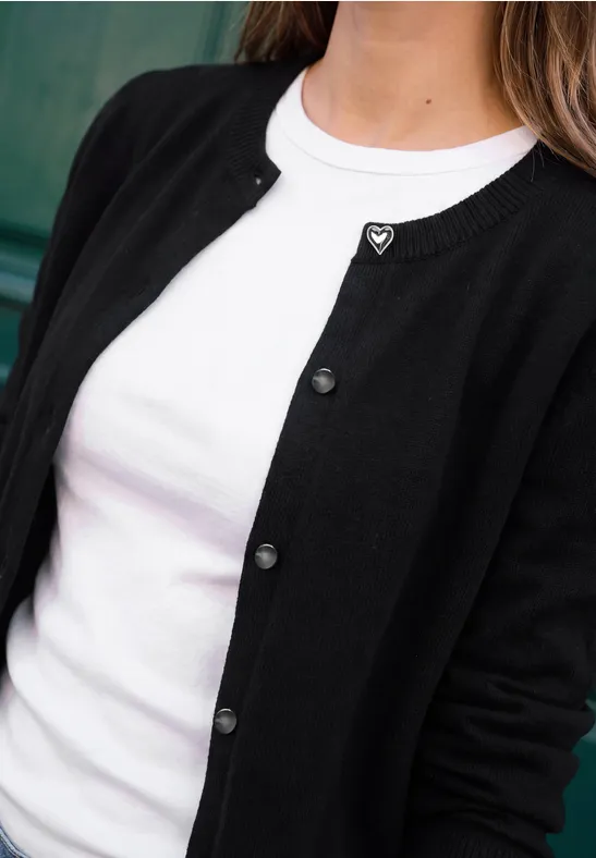 Eine Person trägt ein weißes T-Shirt unter einer schwarzen Strickjacke mit Knöpfen.
