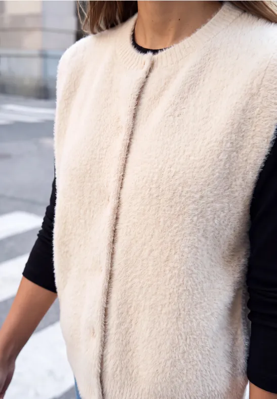 Close-up einer Person mit cremeweißer Teddy-Fleece-Weste über schwarzem Langarmshirt.