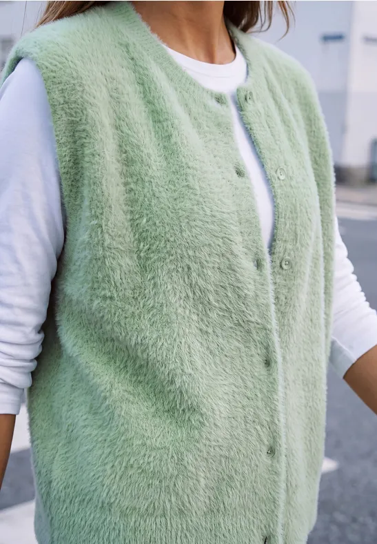 Flauschige, hellgrüne, ärmellose Weste über weißem Langarmshirt.