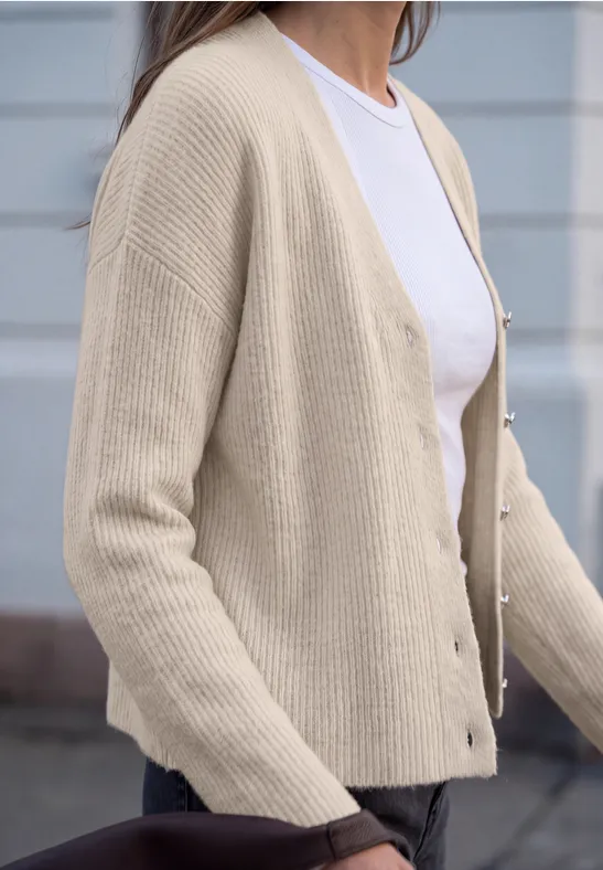 Frau im seitlichen Profil trägt beigen, gerippten Cardigan mit Knöpfen über weißem Shirt.