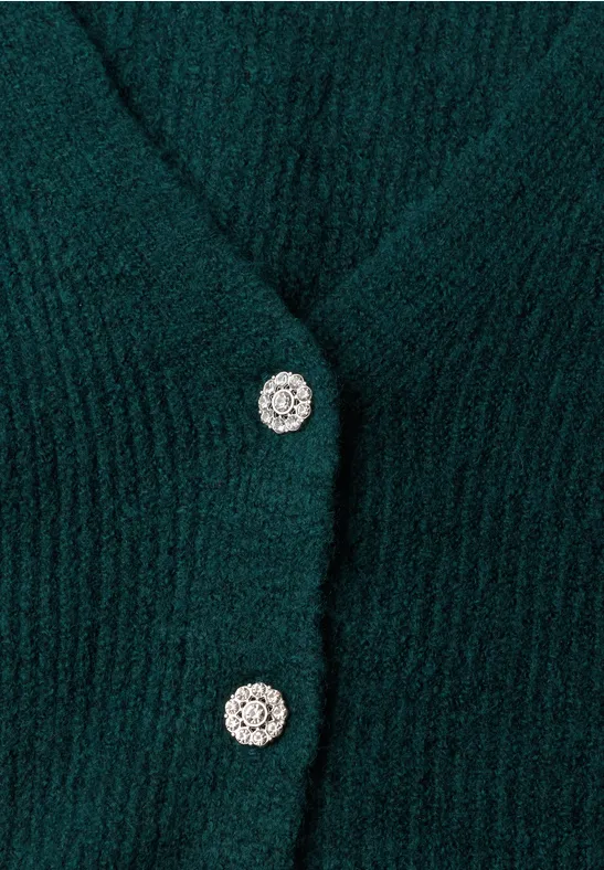 Nahaufnahme eines dunkelgrünen, flauschigen Strickcardigans mit funkelnden silbernen Knöpfen.