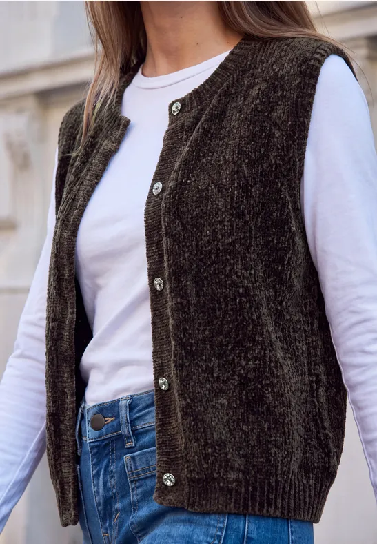 Dame trägt ärmellose Strickweste in Dunkelgrün über weißem Langarmshirt und Jeans.