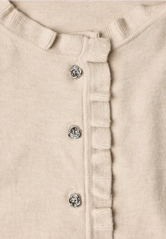 Beige Strickjacke mit Rüschensaum und silbernen Zierknöpfen.