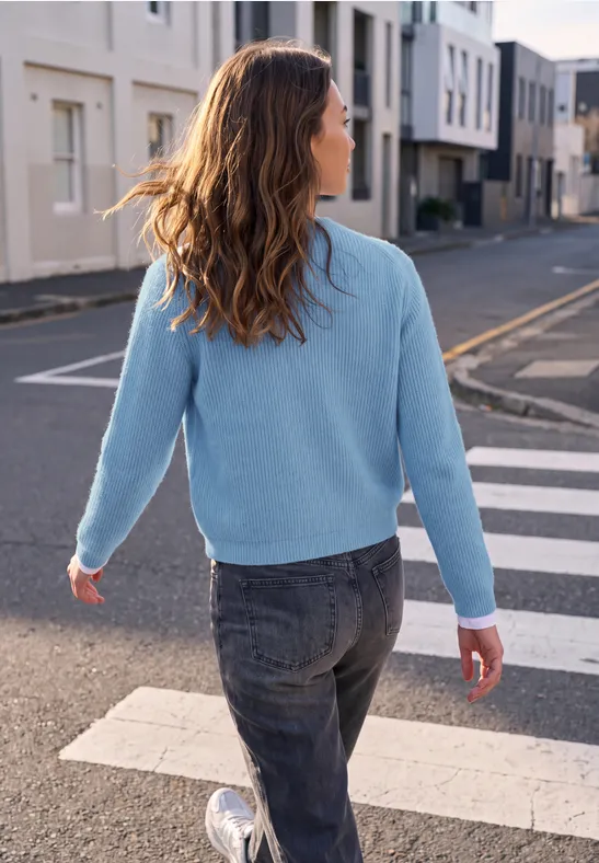 Eine Frau mit hellblauem Pullover und Jeans überquert bei Sonnenschein einen Zebrastreifen in einer modernen Wohnstraße.