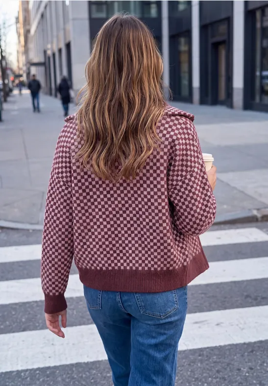 Frau von hinten mit gewelltem Haar, gemustertem Pullover und Jeans, geht mit Coffee-to-go über einen Zebrastreifen.