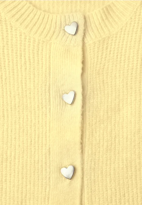 Nahaufnahme eines gelben Strickoberteils mit silbernen herzförmigen Knöpfen.