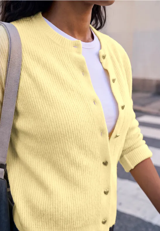 Eine Frau trägt eine gelbe Strickjacke über einem weißen Shirt.