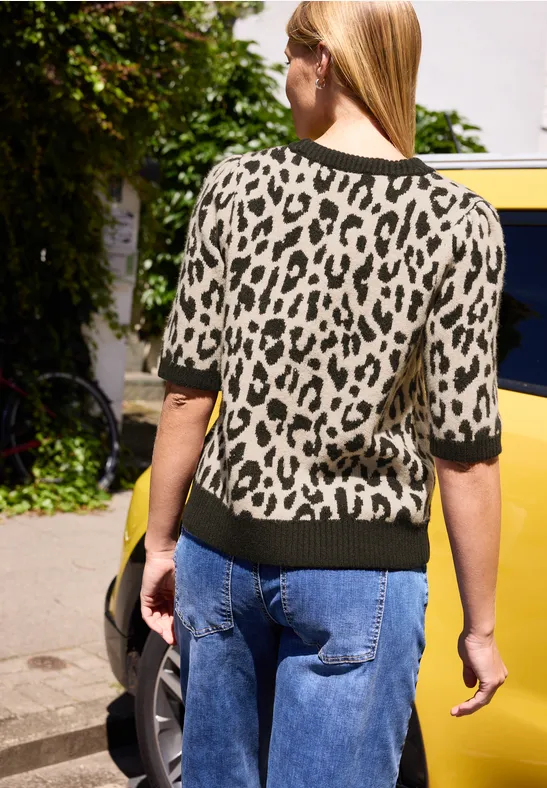 Eine Frau von hinten in Leopardenpullover, Jeans und Handtasche, geht an einem gelben Auto vorbei.