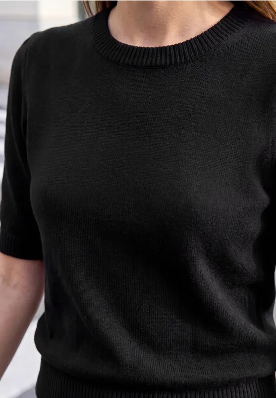 Eine Person trägt ein schlichtes schwarzes Kurzarmshirt.