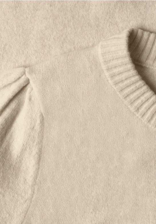 Nahaufnahme eines cremefarbenen Strickpullovers mit geripptem Rundhalsausschnitt und leicht gepufften Ärmeln.