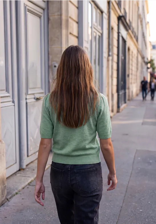 Frau in grünem Pullover und Jeans geht eine Stadtstraße mit historischen Gebäuden entlang.