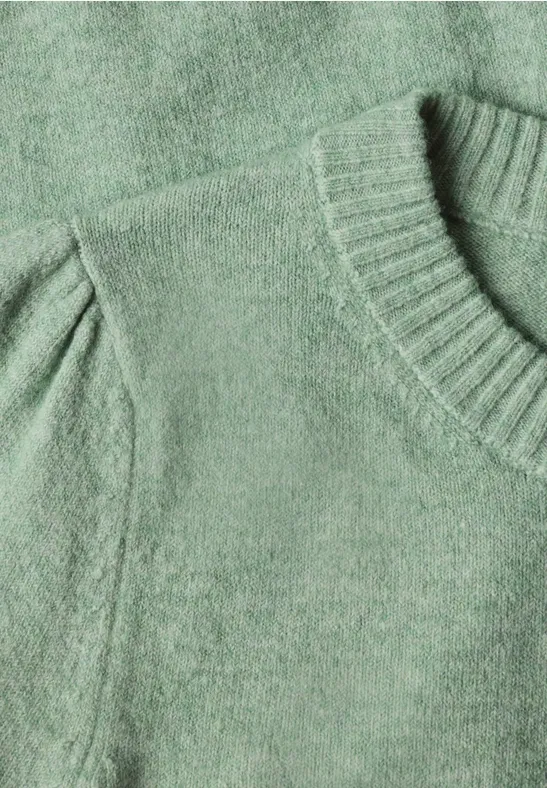 Nahaufnahme eines grünen Strickpullovers mit Rundhalsausschnitt und leichten Puffärmeln.