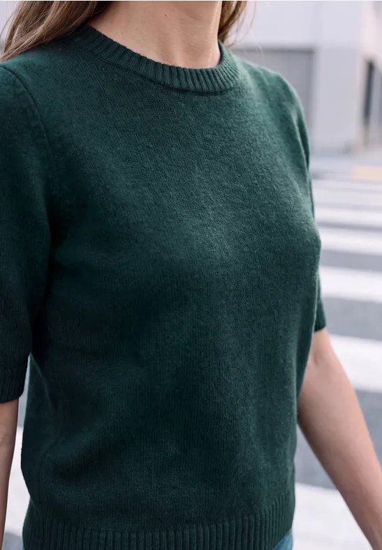 Person trägt dunkelgrünen Kurzarm-Strickpullover, stehend auf einem Zebrastreifen.
