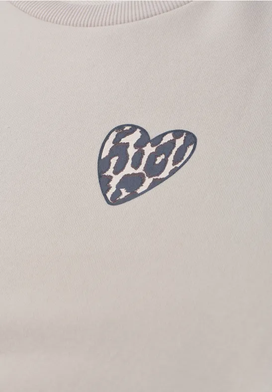 Beżowy T-shirt z małym czarno-białym nadrukiem w kształcie serca z motywem lamparta na piersi.