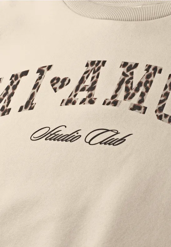 Beiger T-Shirt-Ausschnitt mit Leopardenmuster-Print 'MI-AMU' und darunter Schriftzug 'Studio Club'.