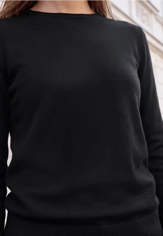 Eine Person trägt einen schlichten schwarzen Pullover, nur der Oberkörper ist zu sehen.