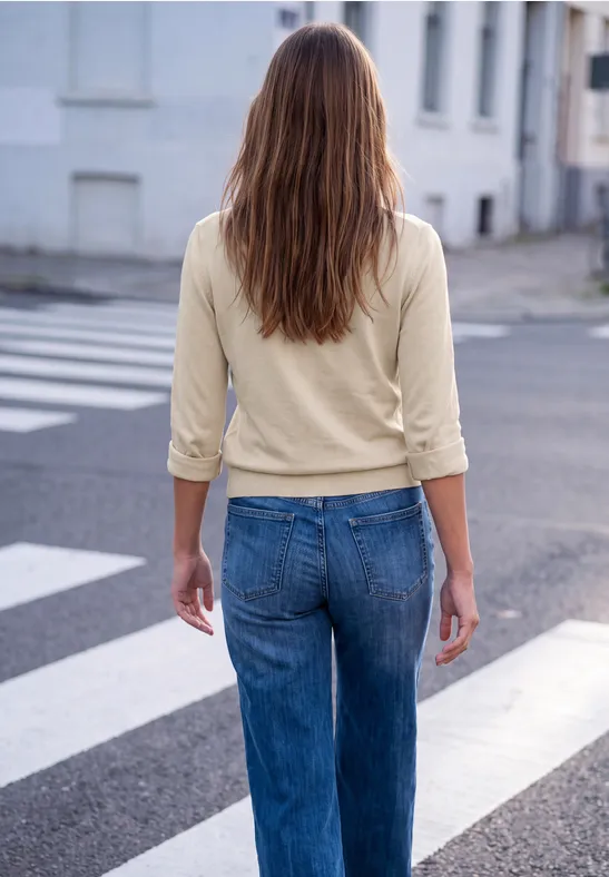 Frau mit langen braunen Haaren in beiger Bluse und blauen Jeans überquert einen Zebrastreifen.