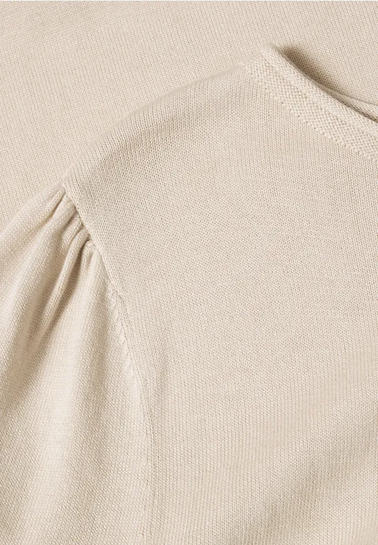 Beige Strickoberteil mit gerafftem Puffärmel in Nahaufnahme.