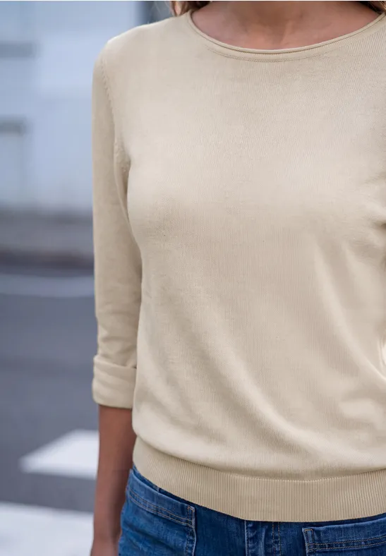 Person trägt beigefarbenes 3/4-Arm-Shirt und blaue Jeans, Oberkörper frontal.