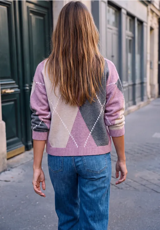 Eine Frau mit langem Haar trägt einen gemusterten Pullover und Jeans und geht durch eine Stadtstraße.