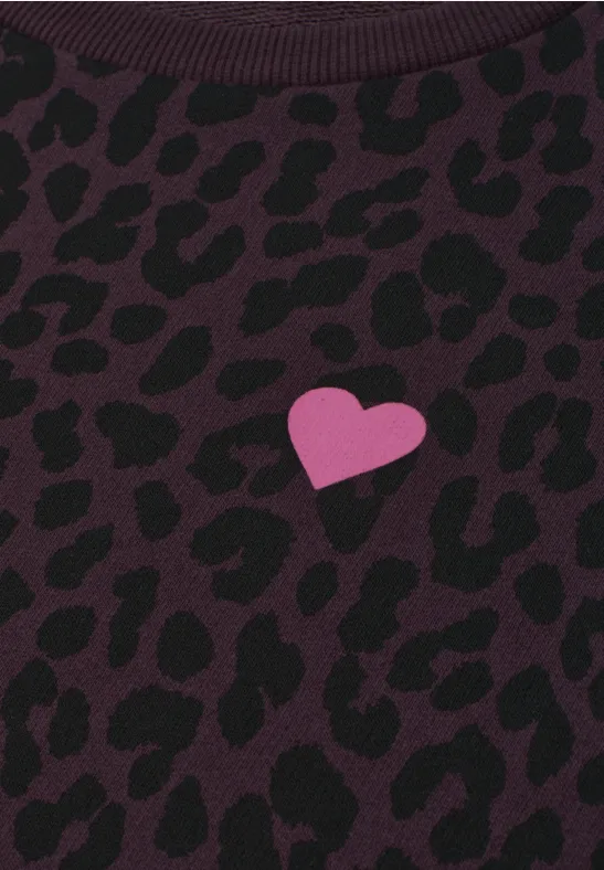 Nahaufnahme eines dunkellila Stoffes mit schwarzem Leopardenmuster und kleinem pinken Herz.