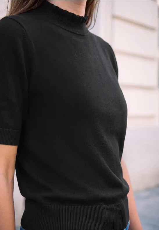 Nahaufnahme einer Frau in elegantem schwarzen Kurzarmstrickpullover mit Rollkragen und Rüschenkante.