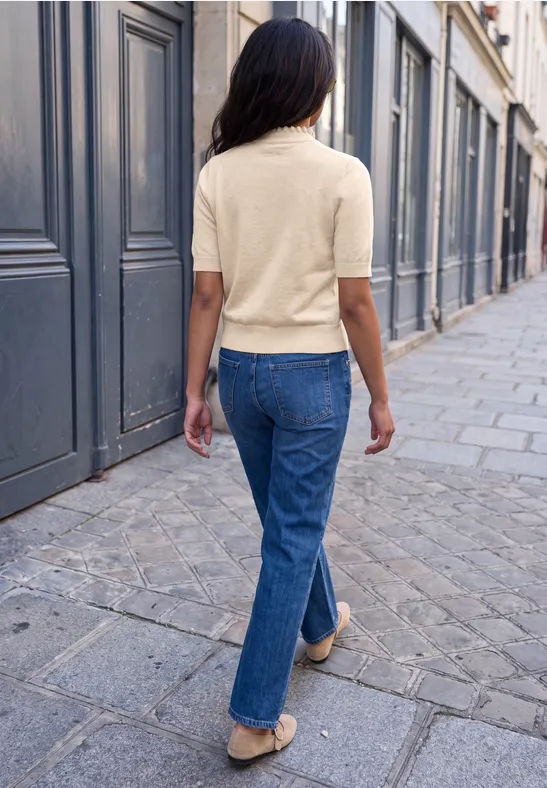 Eine Frau in Jeans und kurzärmligem Pullover geht eine gepflasterte Stadtstraße entlang.