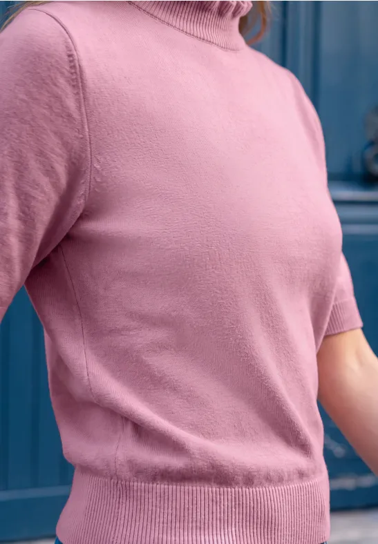 Nahaufnahme einer Person in einem pinkfarbenen Kurzarm-Rollkragenpullover vor einer blauen Tür