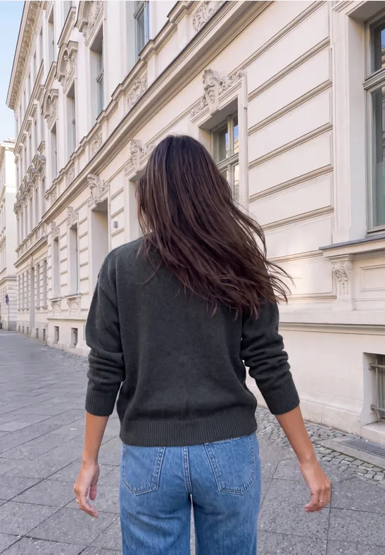 Frau mit langen Haaren läuft eine Straße entlang, von hinten gesehen.