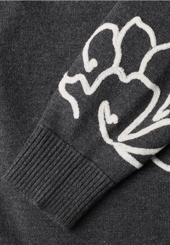 Nahaufnahme eines schwarzen Strickärmels mit weißem Blumenmuster und Rippbündchen