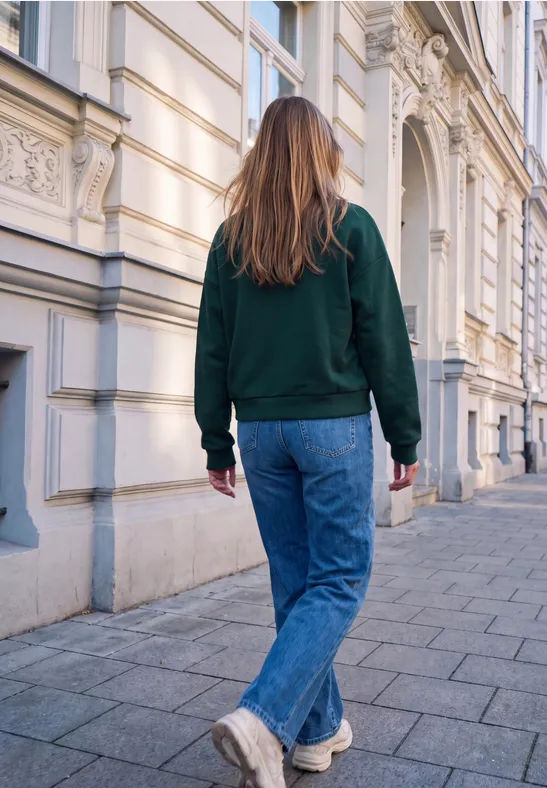 Kobieta w zielonym swetrze idzie miejską ulicą obok zabytkowych kamienic.