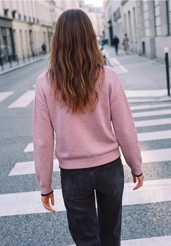 Eine Person mit rosa Pullover und dunkler Hose überquert einen Zebrastreifen in der Stadt.