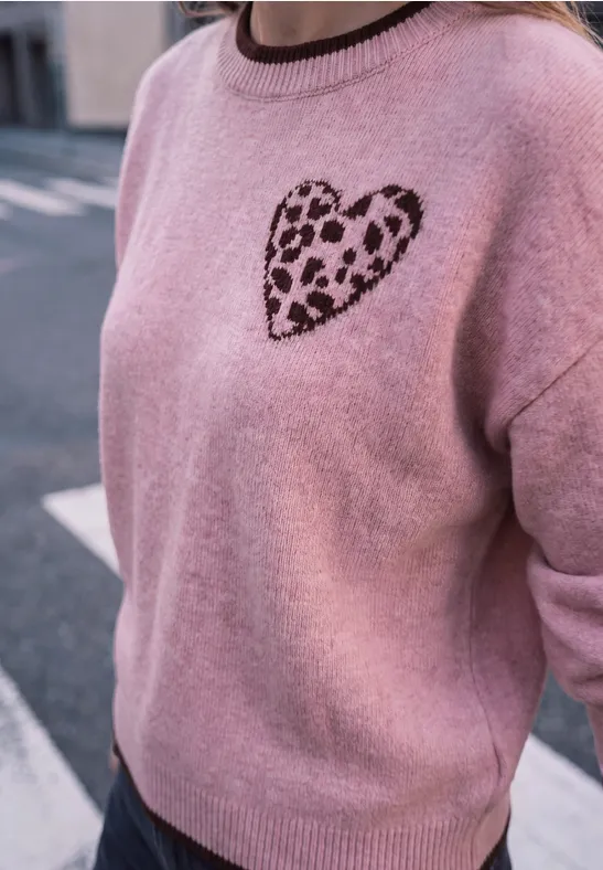 Eine Person trägt einen rosafarbenen Pullover mit Leopardenmuster-Herz auf der Brust.